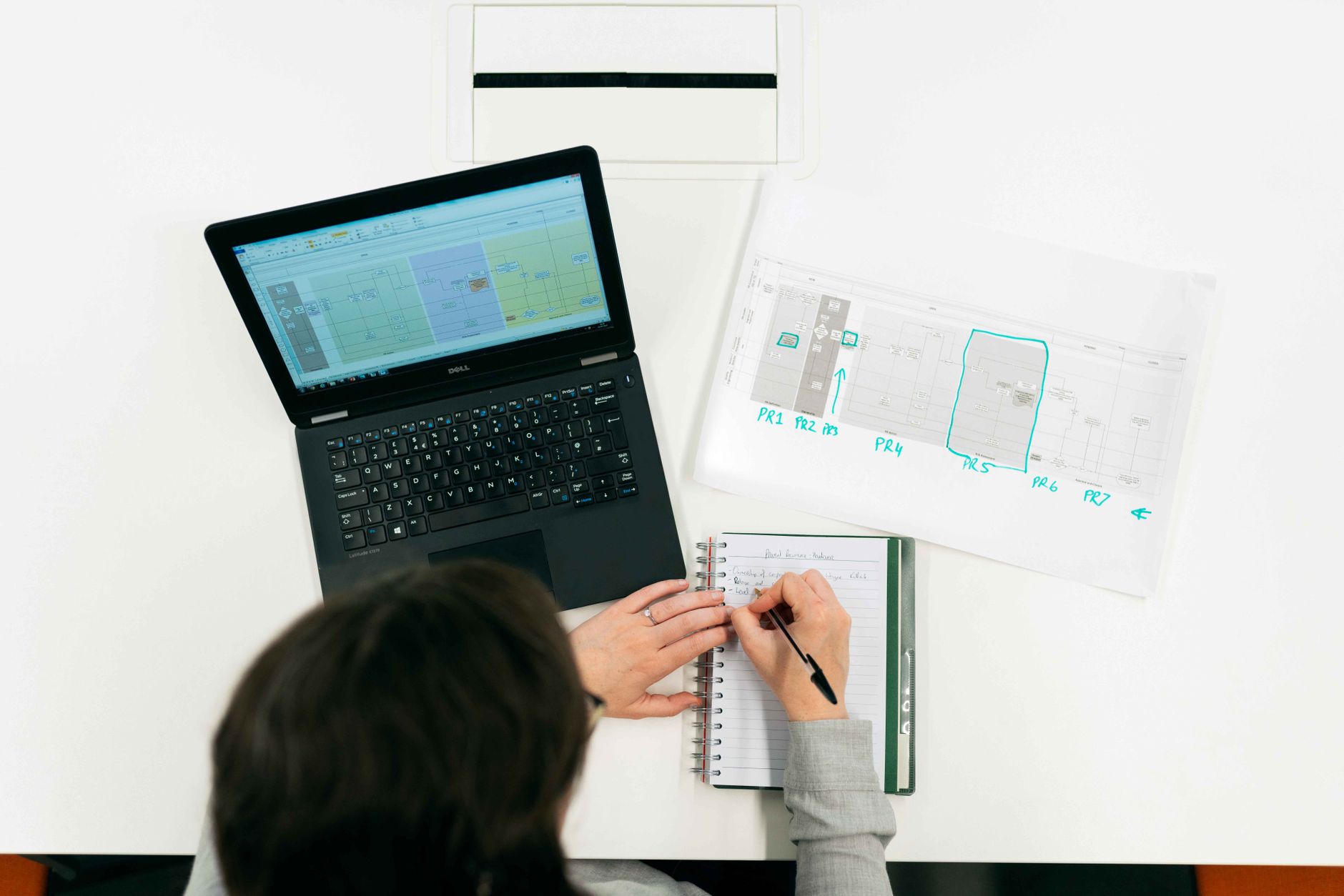 A person taking notes from data on a laptop screen in an office setting.