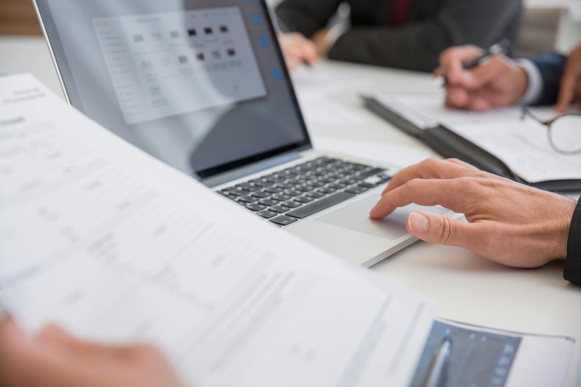 Close-up of hands working on documents and a laptop in an office setting.