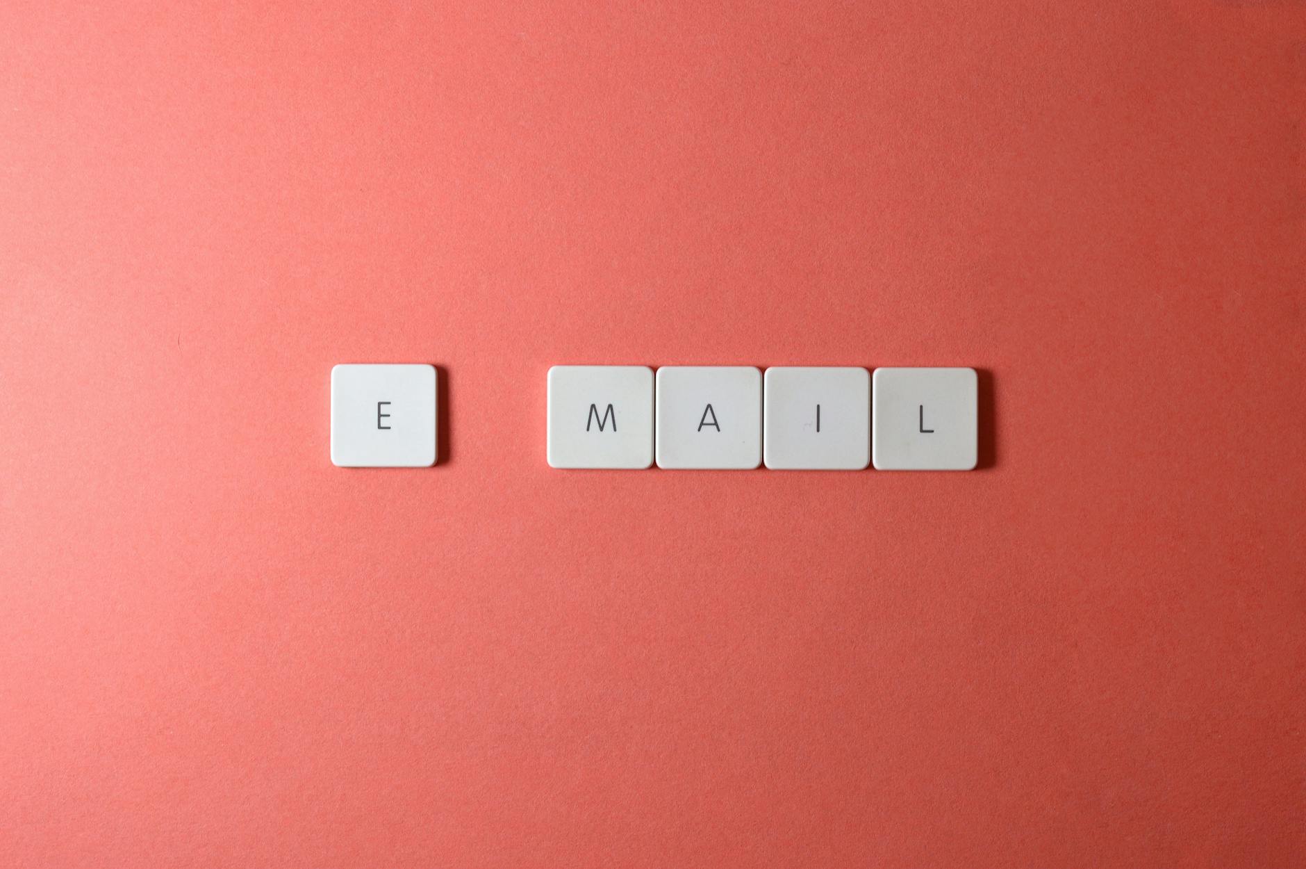 Flat lay of keyboard letter tiles spelling email on coral backdrop.